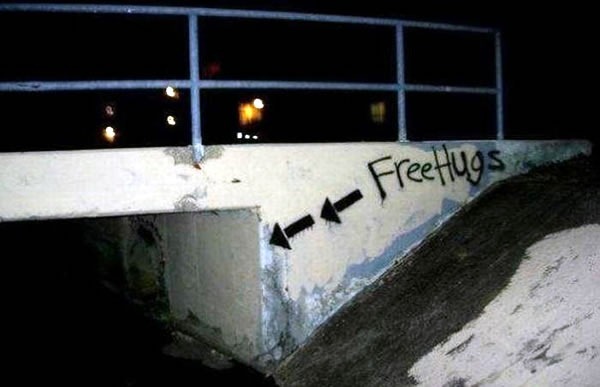 Dark tunnel under a small footbridge labelled in spraypaint: "Free hugs"