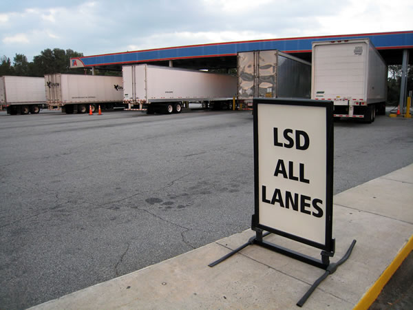 Trucks at a gas station with a sign in the foreground that reads “LSD ALL LANES”
