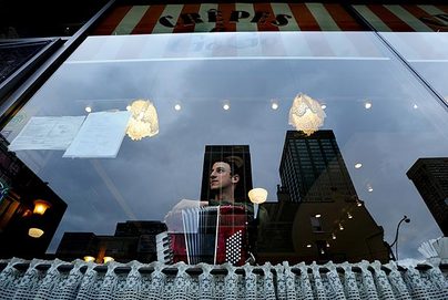 Ronen Segall with his accordion, seen through the front window of a restaurant.