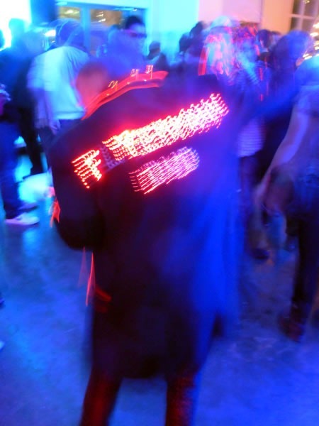 Flyerman, from behind, with his trademark jacket studded with LEDs that spell out "Flyerman DVD"