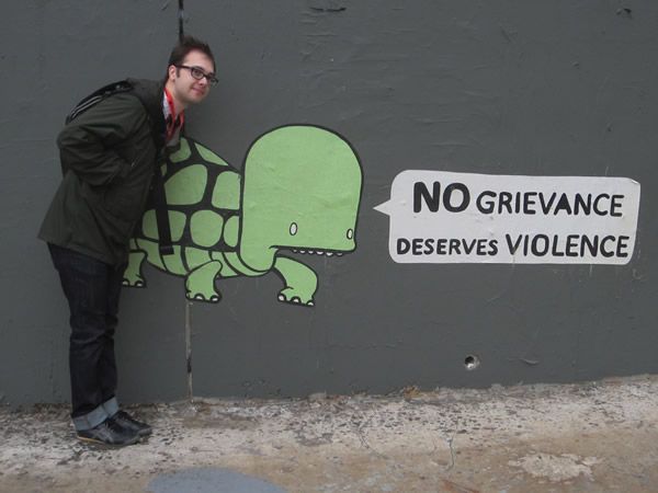 Edward Ocampo-Gooding poses beside the "No grievance deserves violence" graffito