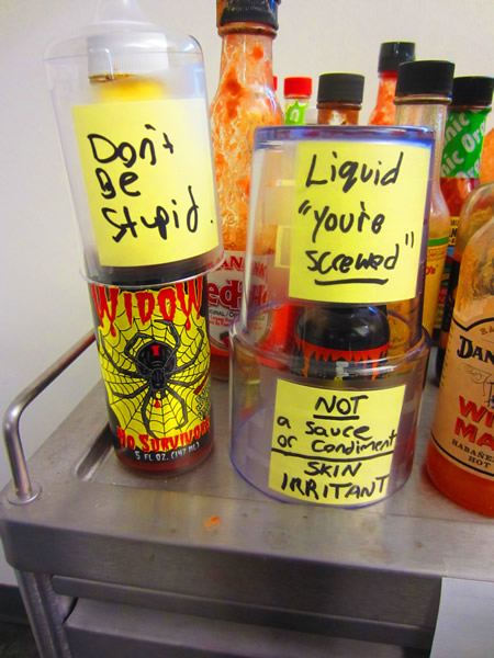 Close-up of two bottles of hot sauce. One is labelled "Don't be stupid", the other has two labels: "Liquid 'you're screwed'" and "Not a sauce or condiment - skin irritant"