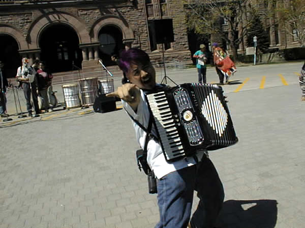 Joey deVilla with accordion in front of Queen’s Park, Toronto, “throwing the horns.”