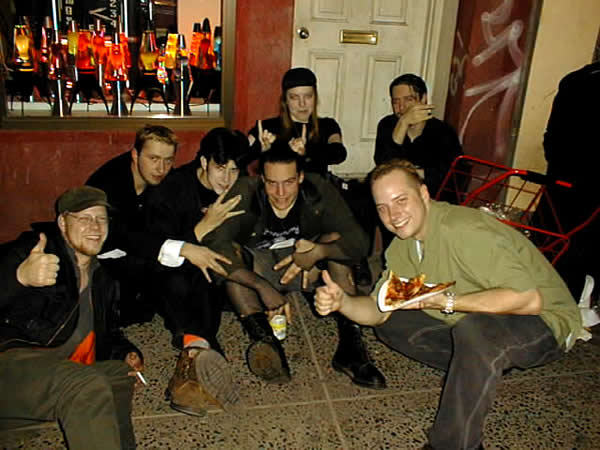 A crowd of young goths/punks/alt-rock fans outside the pizza place, giving a thumbs-up.