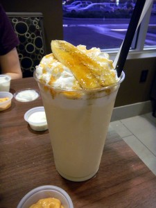 Bananas Foster milkshake in a large glass with a straw, covered in whipped cream and a caramelized banana
