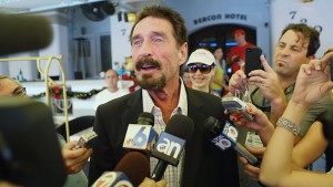 John McAfee speaks to a throng of news reporters with microphones