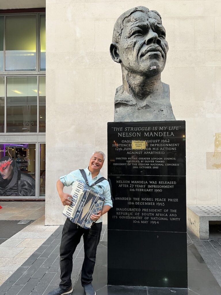Joey deVilla poses with his accordion beside a bust of Nelson Mandela near Southbank Centre, London, UK.