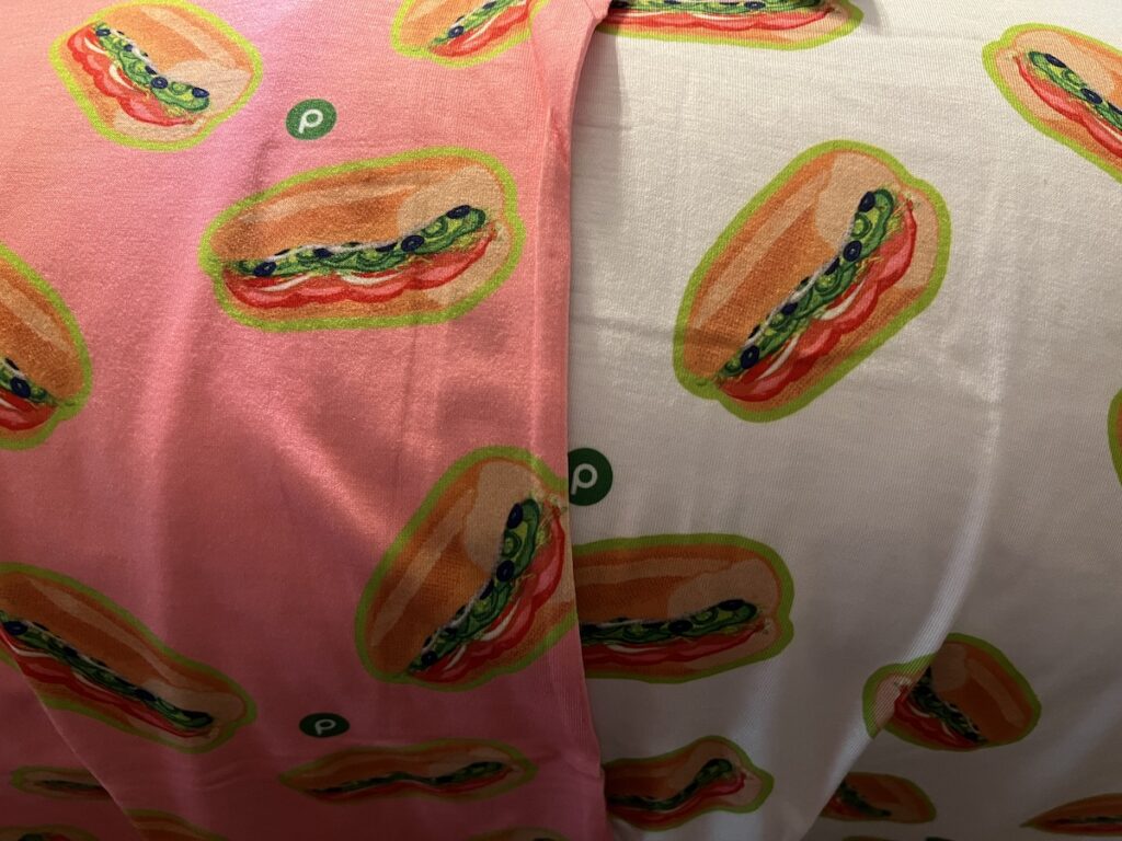 Pink and white t-shirts covered with images of Publix subs and the Publix logo