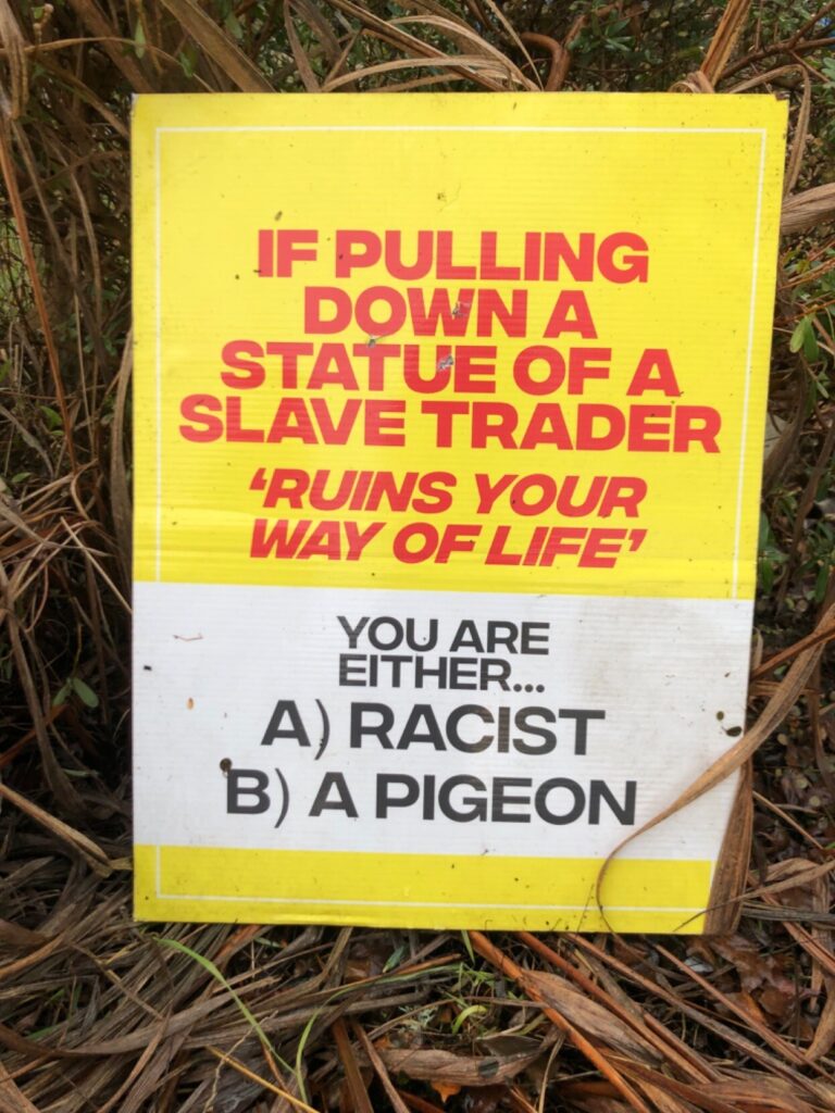 Sign that reads: “If pulling down a statue of a slave trader ‘ruins your way of life,’ you are either (a) a racist (b) a pigeon.”