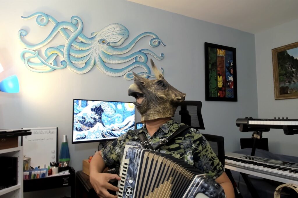 Joey deVilla in his home office, playing accordion in a triceratops mask.