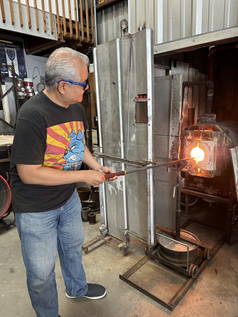 Joey pushes a punty (glass-making rod) into a glass furnace.